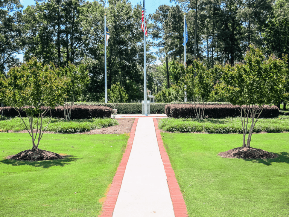 A walkway in the middle of a park with trees and flags.
