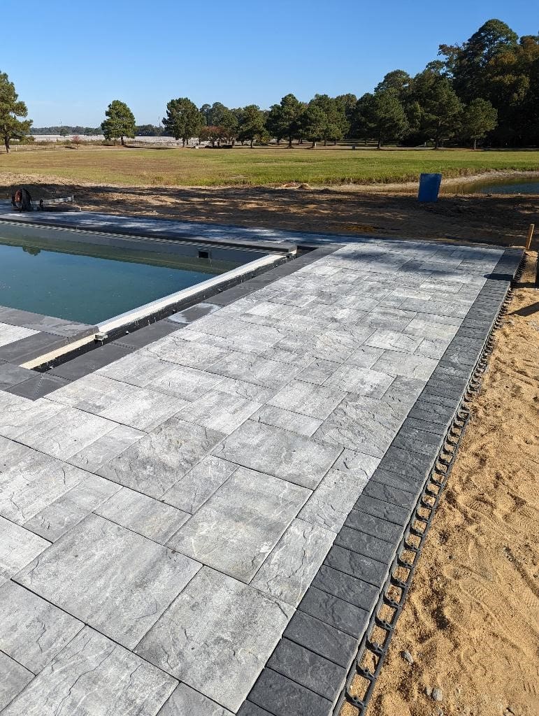 A pool with a stone walkway and a concrete slab.