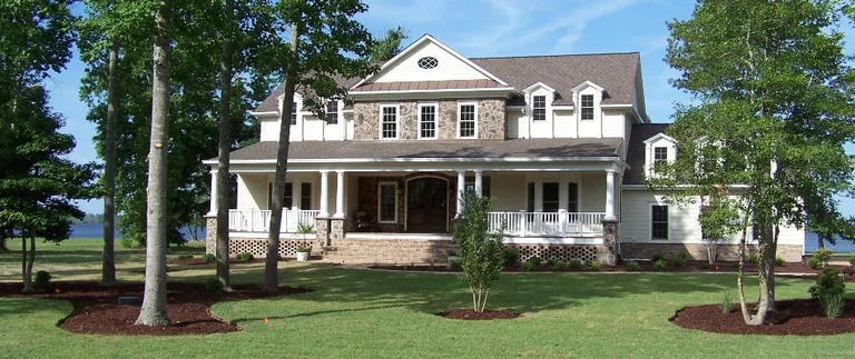 Large house with porch surrounded by trees.