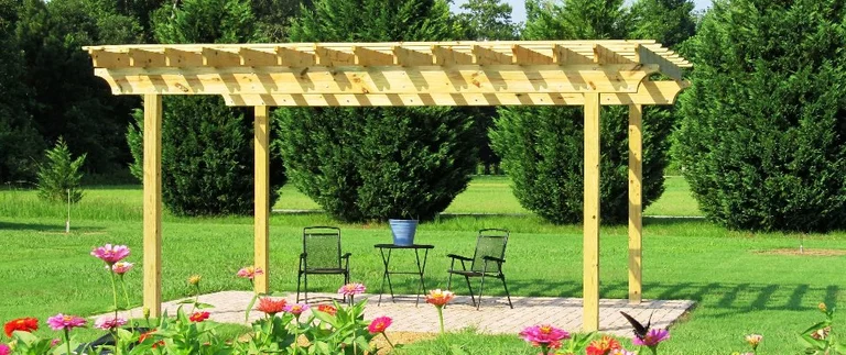 Wooden pergola with chairs on grassy lawn.