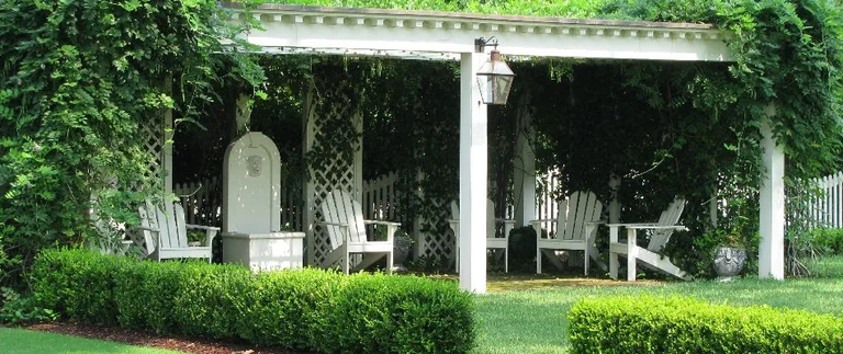 Garden pergola with chairs and lush greenery.