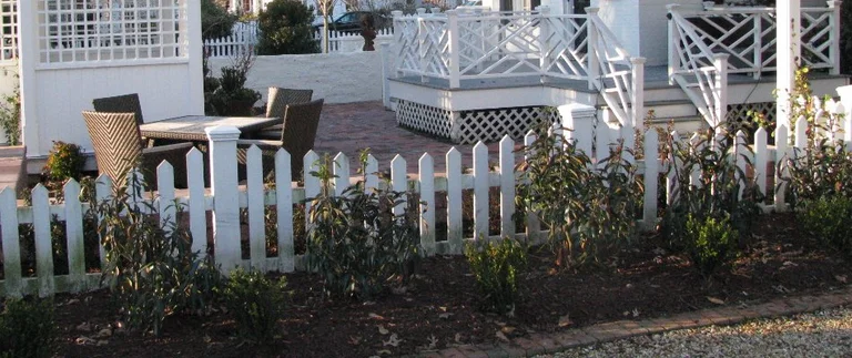 White picket fence and patio furniture outside.