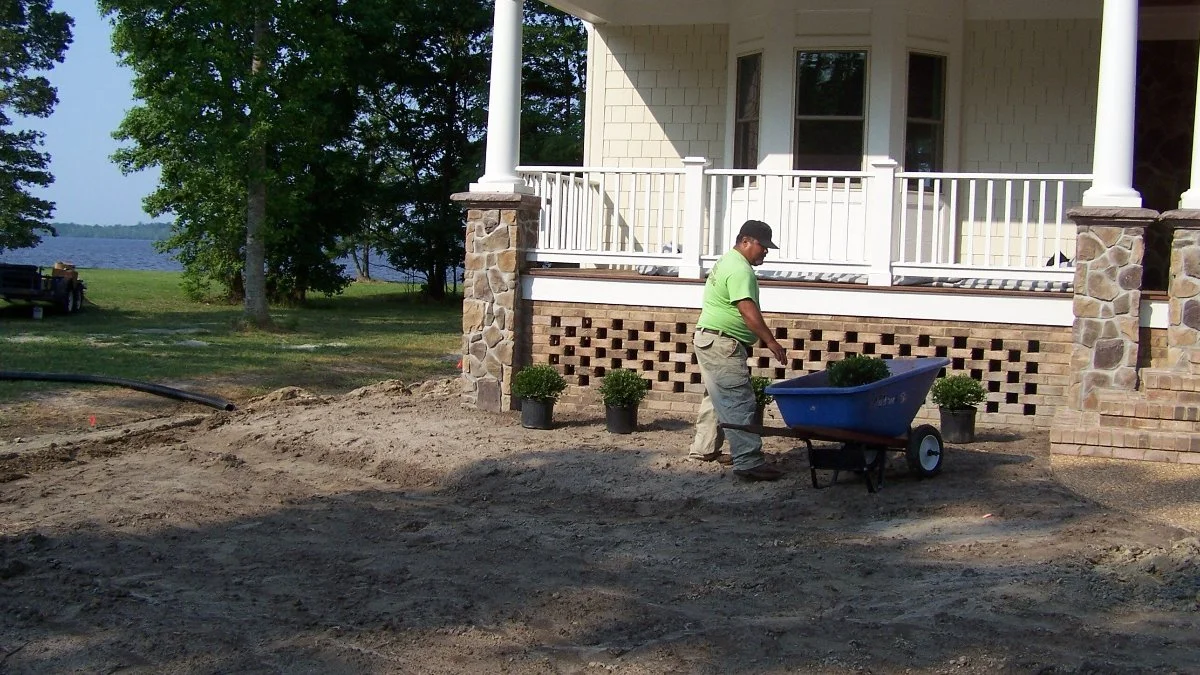 Person gardening with wheelbarrow near house.
