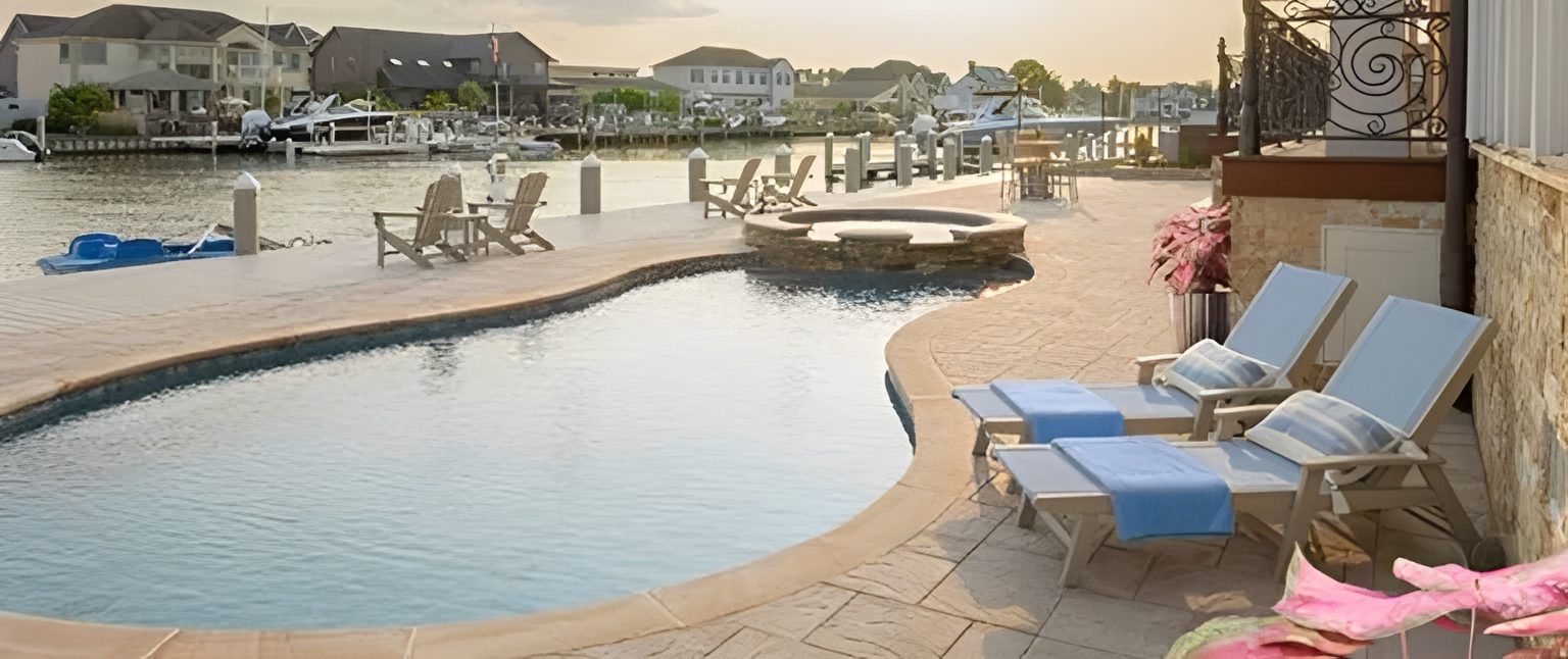 Poolside view with loungers and waterfront backdrop.